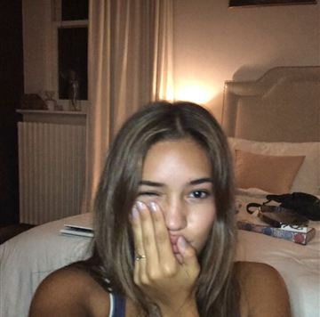 Young woman on her bed at night covering her mouth while staring at her phone