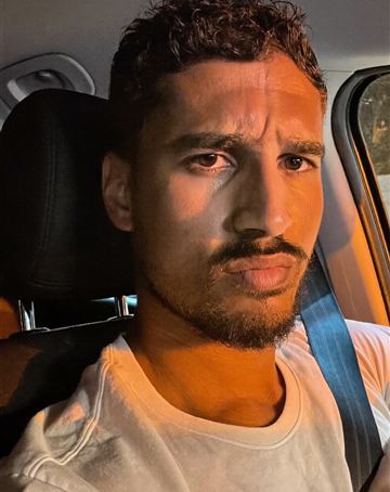 Man in the driver seat of a car at night, lit orange by a streetlight, staring seriously at the camera