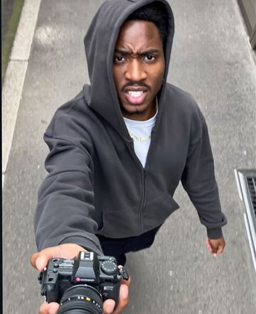 Man in a hoodie on the street pointing a camera at the viewer