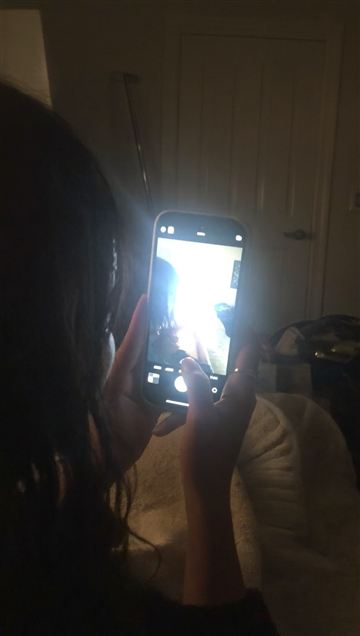 Over the shoulder view of a glowing phone screen in a dark living room